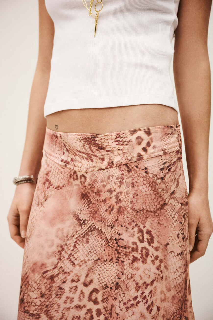 Person wearing a white top and pink pattern skirt on a plain background
