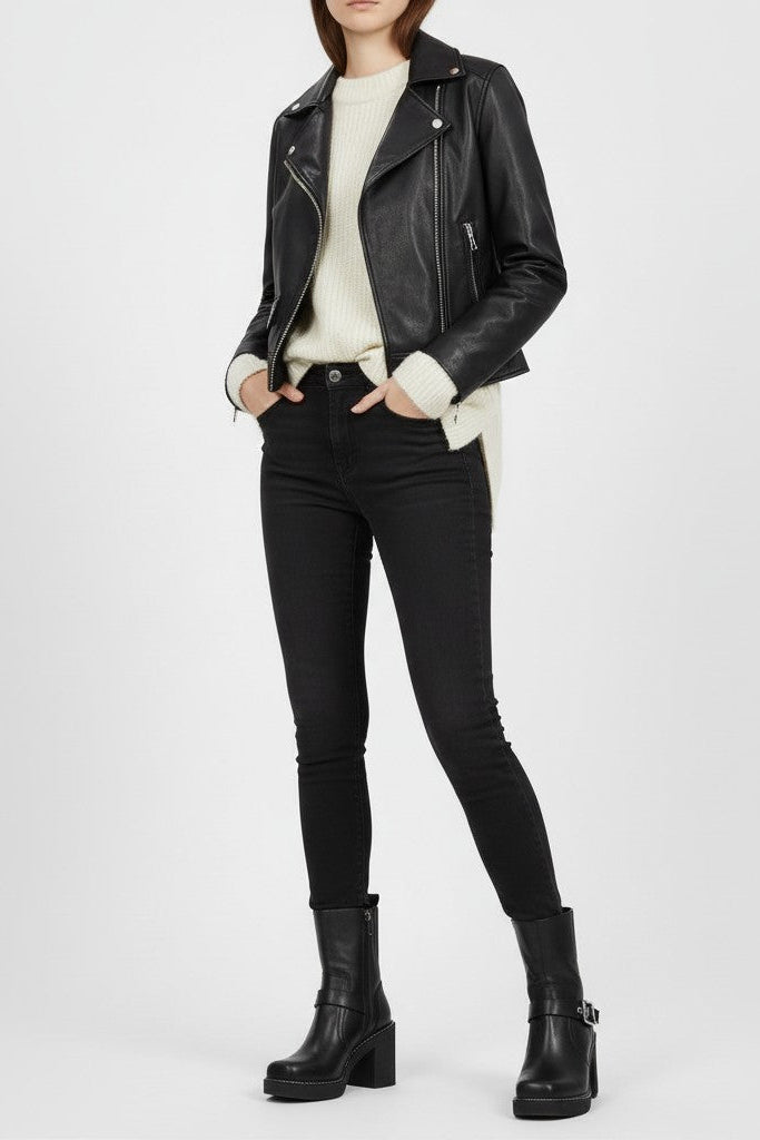Woman wearing a black leather jacket, white shirt, black pants, and black boots on a plain background