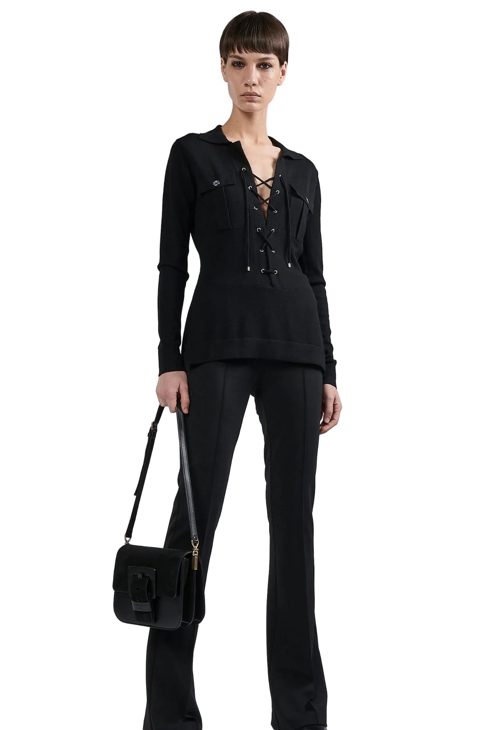 Woman wearing a black outfit with a jacket and pants, holding a black handbag on a white background.