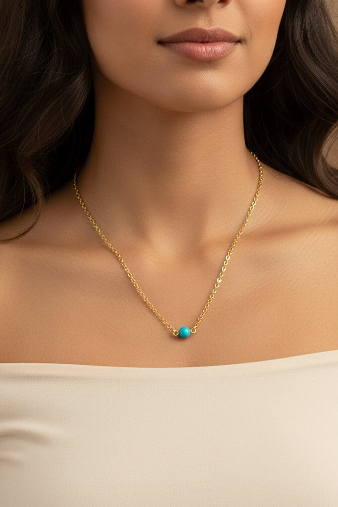 Woman wearing a gold necklace with a turquoise pendant against a neutral background.