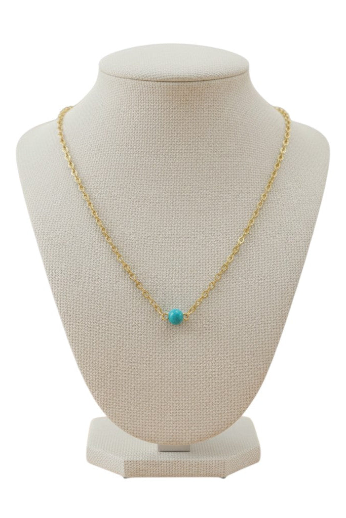 Gold chain necklace with a turquoise pearl on a canvas display against a white background.