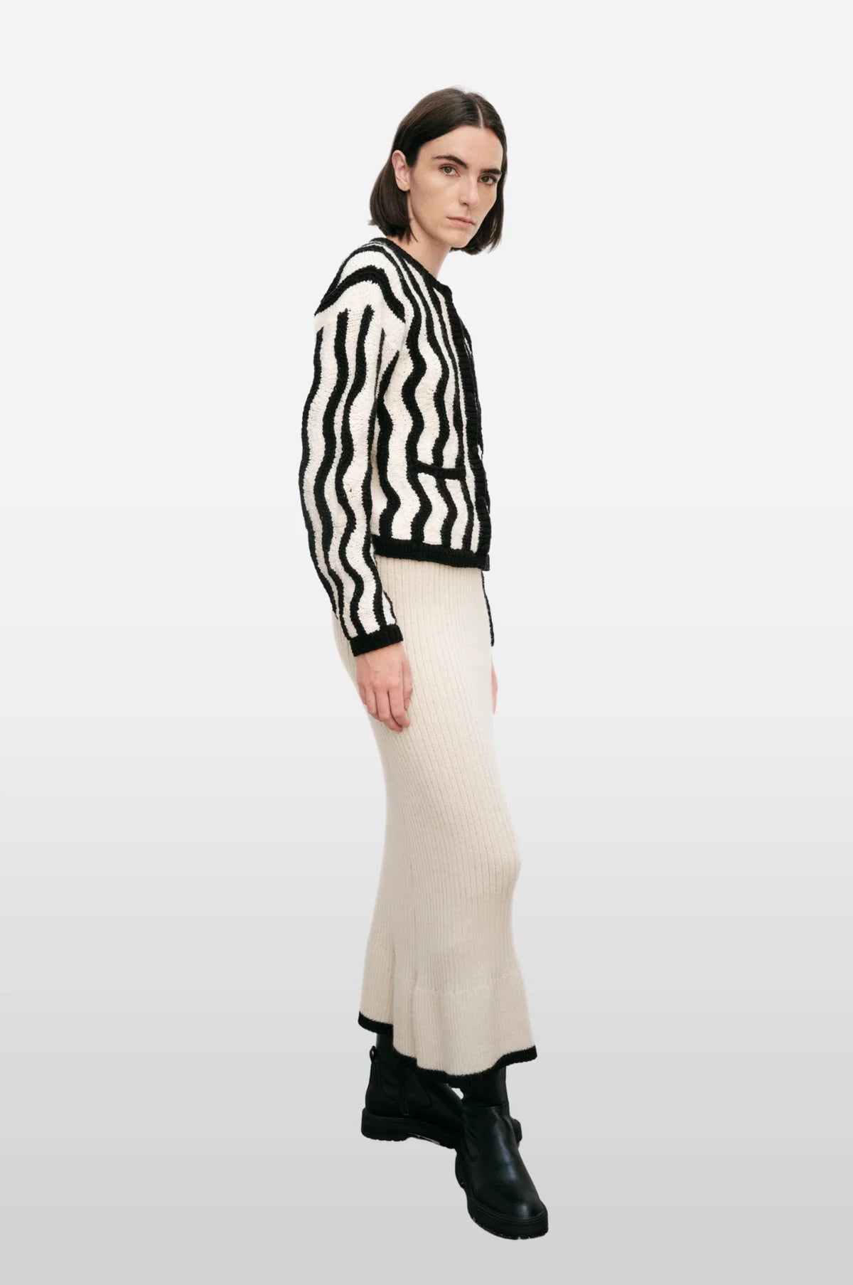 Woman wearing a black and white striped sweater with a long beige skirt on a white background.