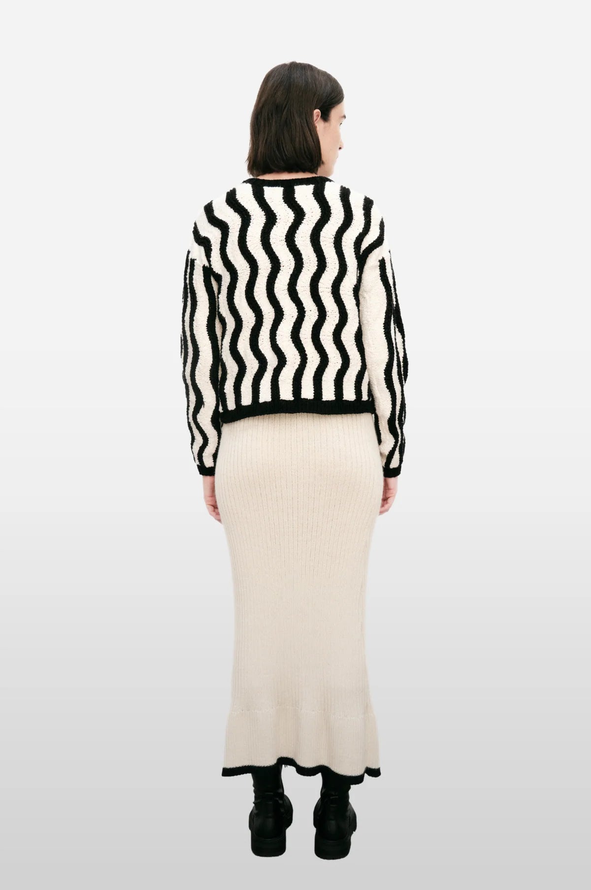 Back of a woman wearing a black and white striped sweater and beige skirt on a white background.