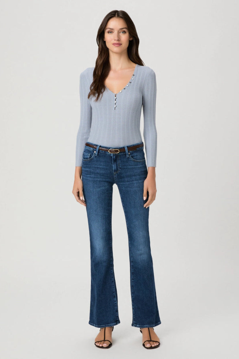 A woman modeling a light blue ribbed long-sleeve henley top and dark blue flare jeans against a plain light gray studio background.