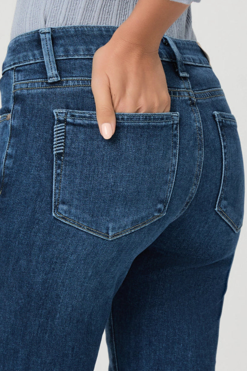Close-up back view of a person wearing dark blue denim jeans, with one hand tucked into the back pocket.