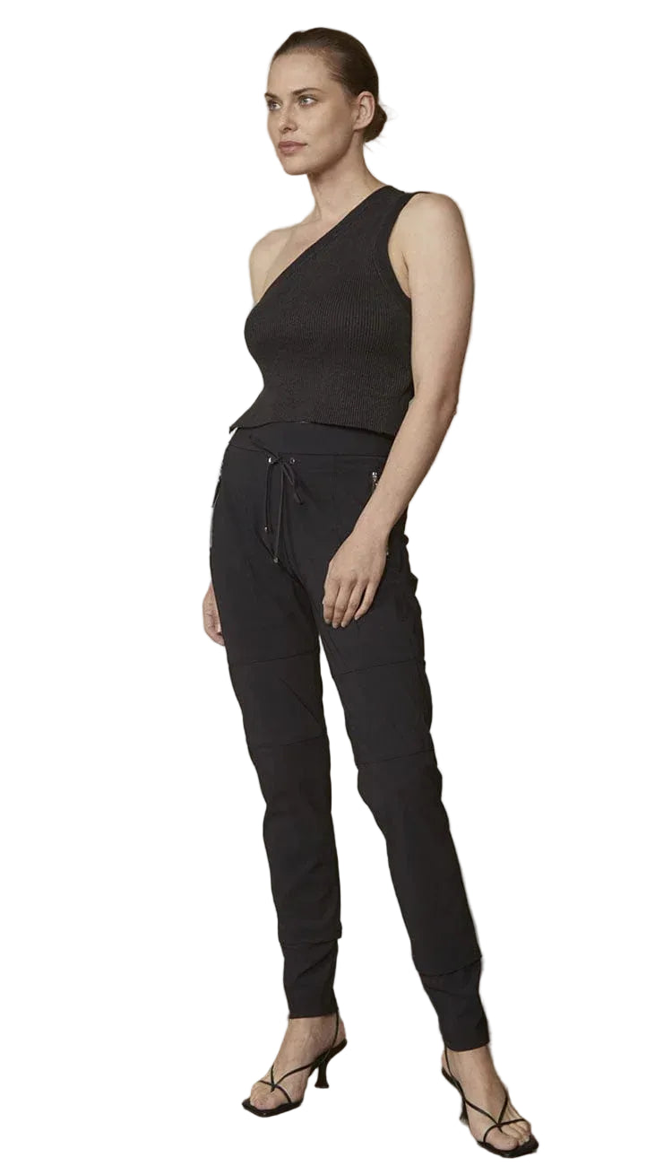 Woman wearing a black one-shoulder top and black drawstring pants against a plain background.