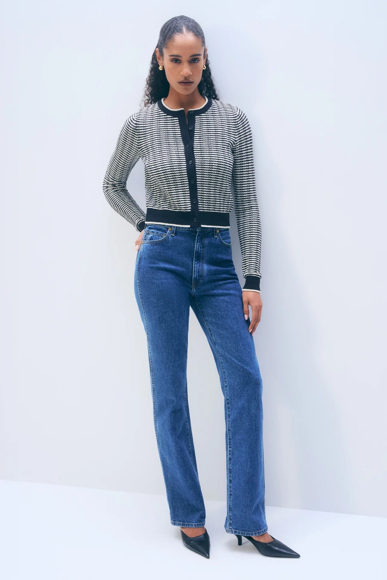 Woman wearing a patterned navy and ivory cardigan with blue jeans against a white background.