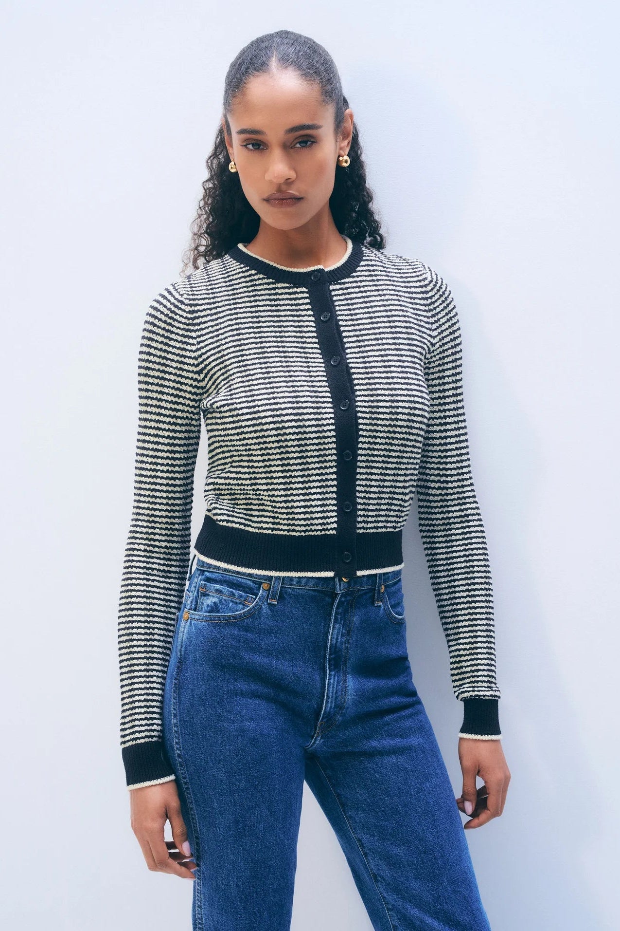 Woman wearing a midnight blue and ivory patterned cardigan with blue jeans against a light gray background.