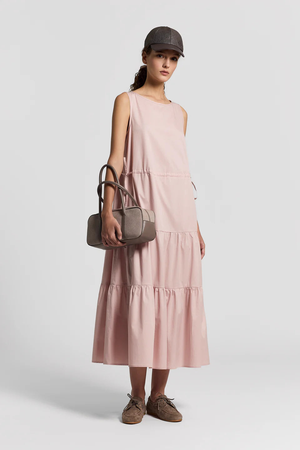 Woman wearing a pink dress, brown cap, and holding a matching handbag on a white background.