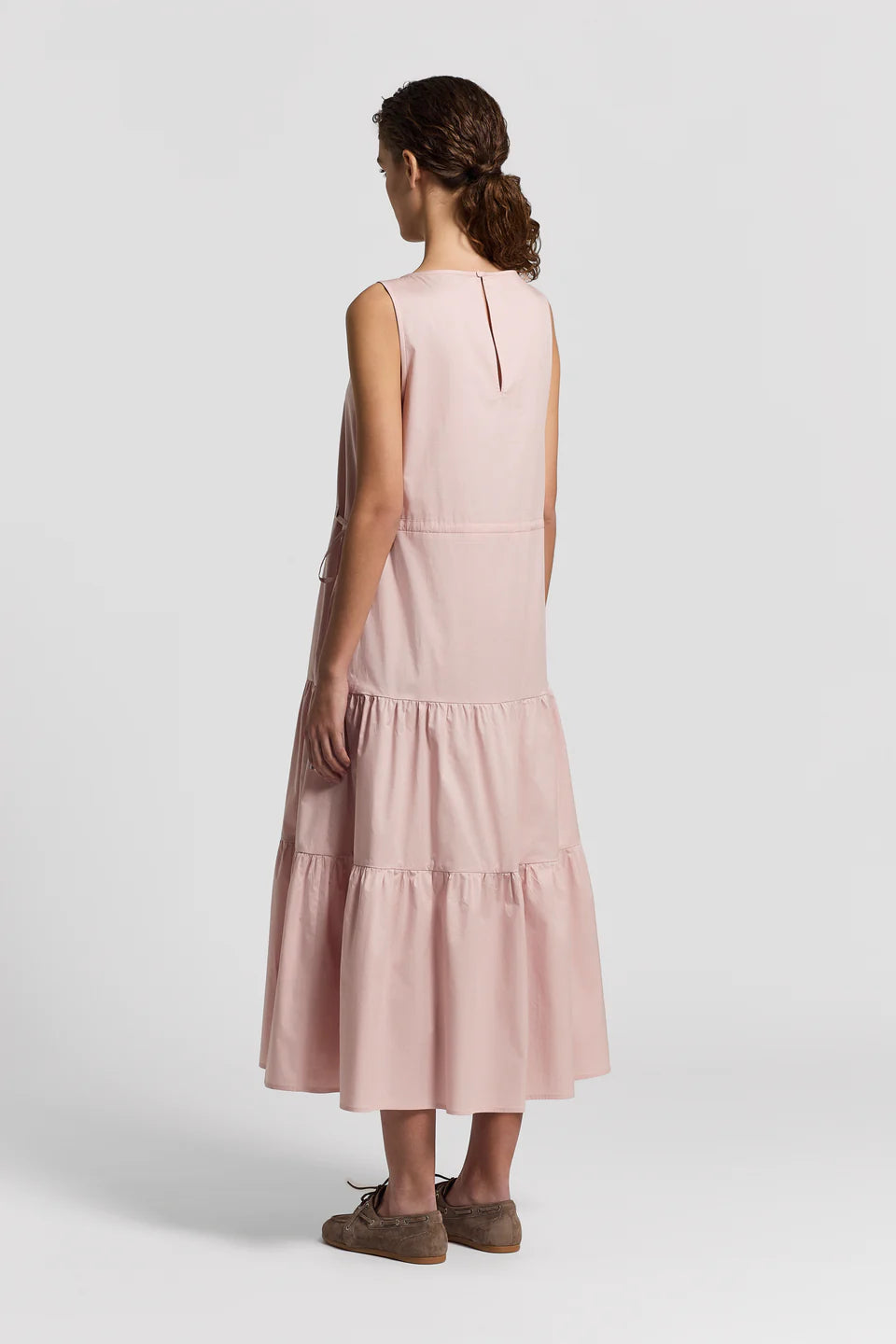 Back of a woman wearing a pink dress with a white background.