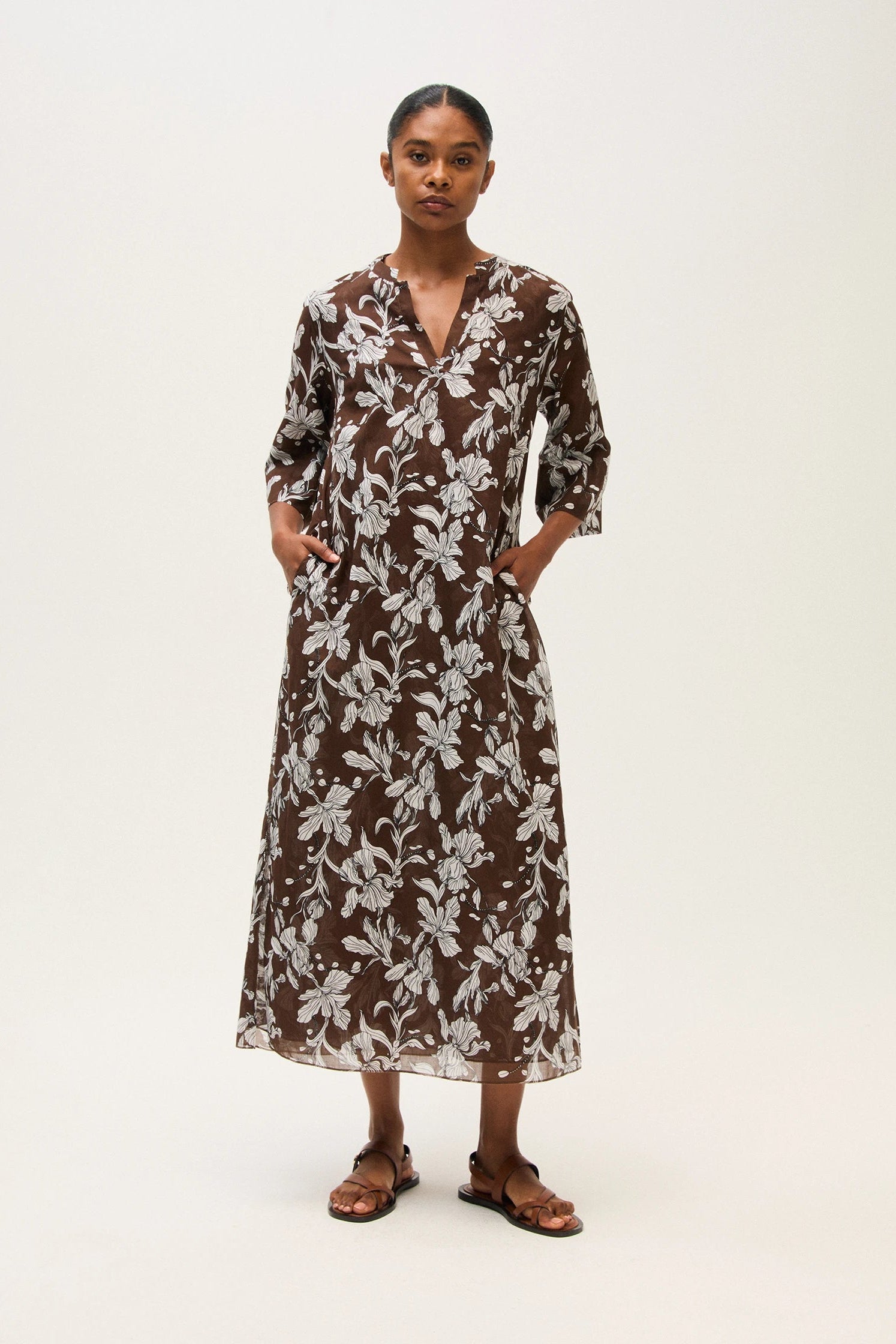 Woman wearing a brown floral dress on a white background.