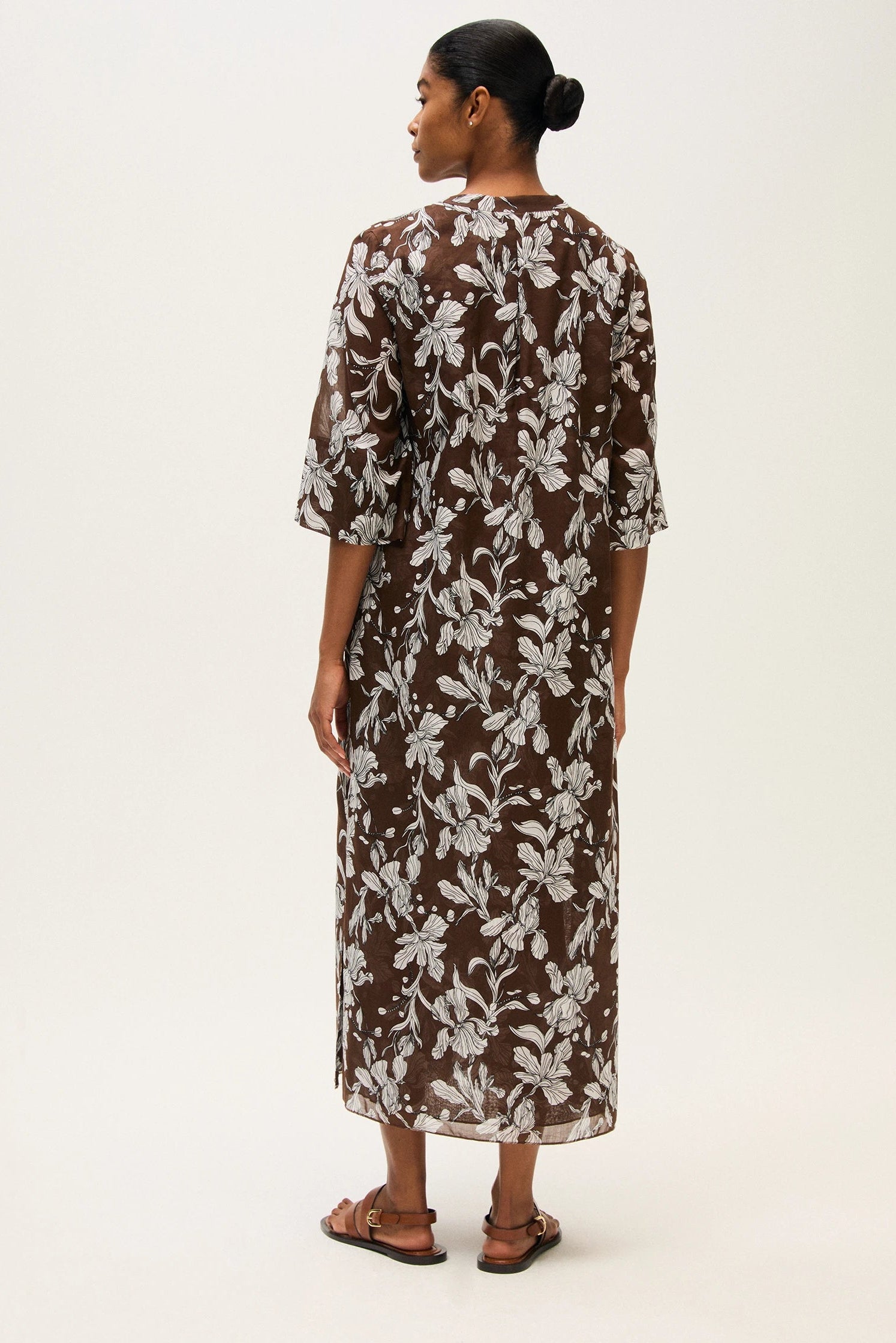 Back of a woman wearing a brown floral dress on a white background.