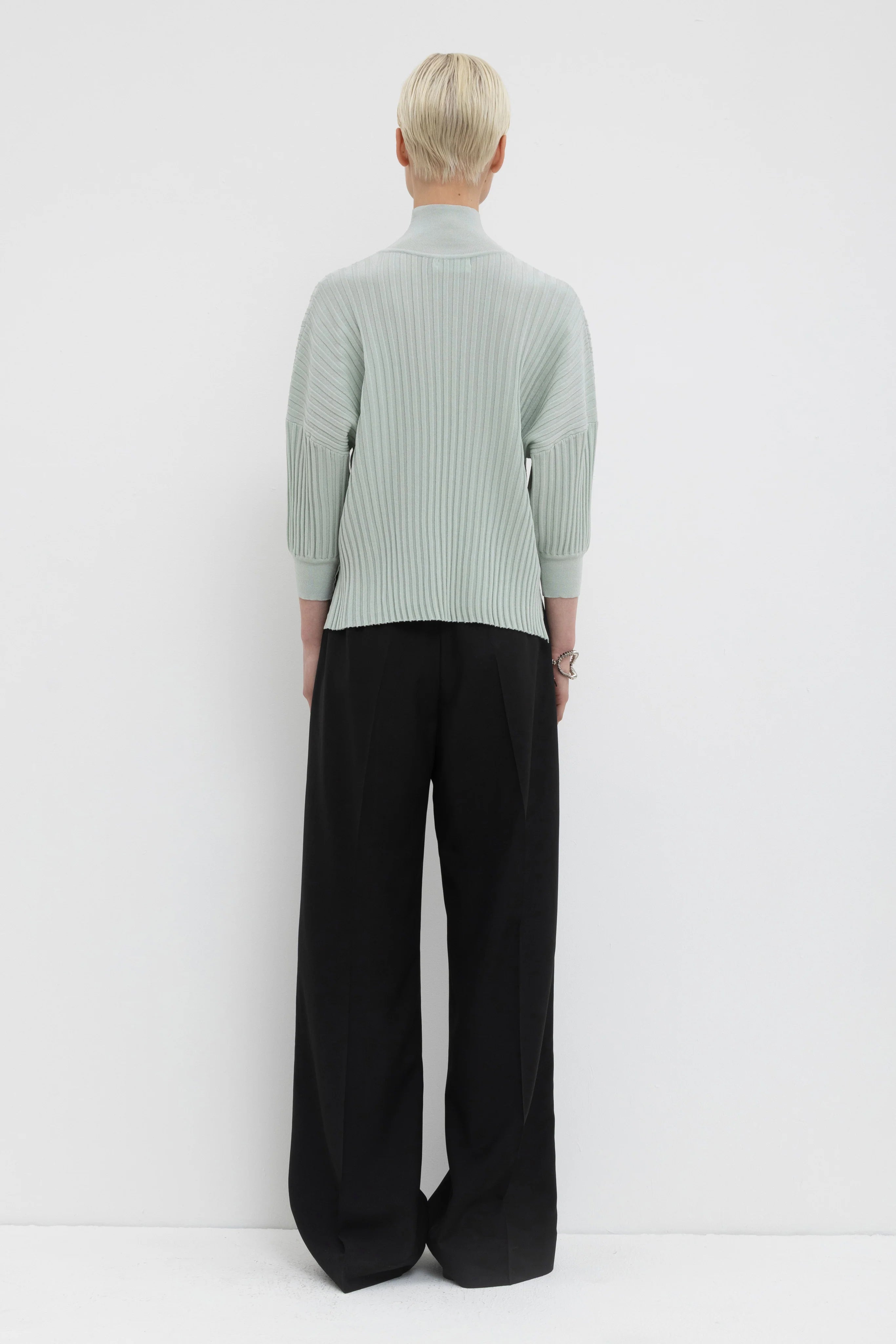 Person wearing a light gray ribbed sweater and black wide-leg pants on a white background