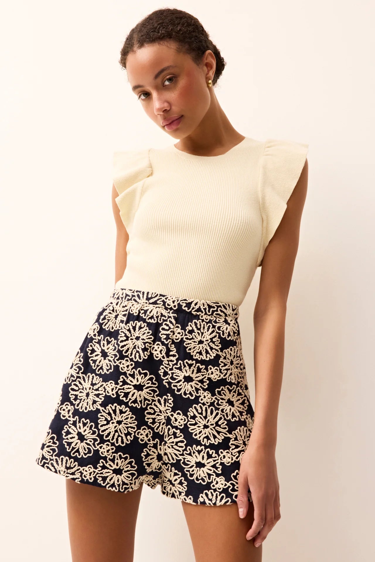 Woman wearing a cream top and navy floral shorts against a white background.