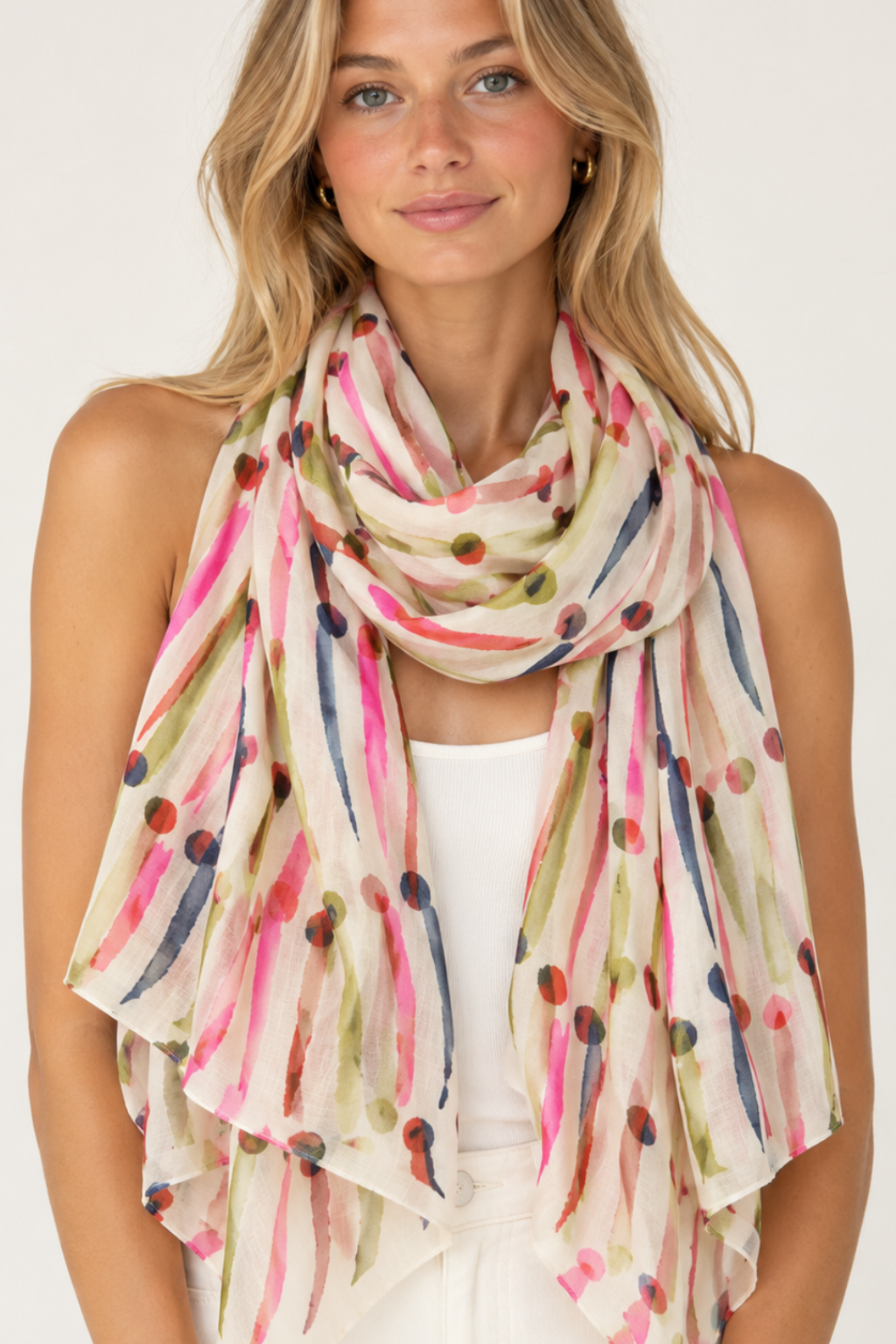 Woman modeling a lightweight cream scarf with a colorful abstract print of pink, blue, green, and brown brushstrokes and dots, paired with a white tank top and white pants against a plain white background.
