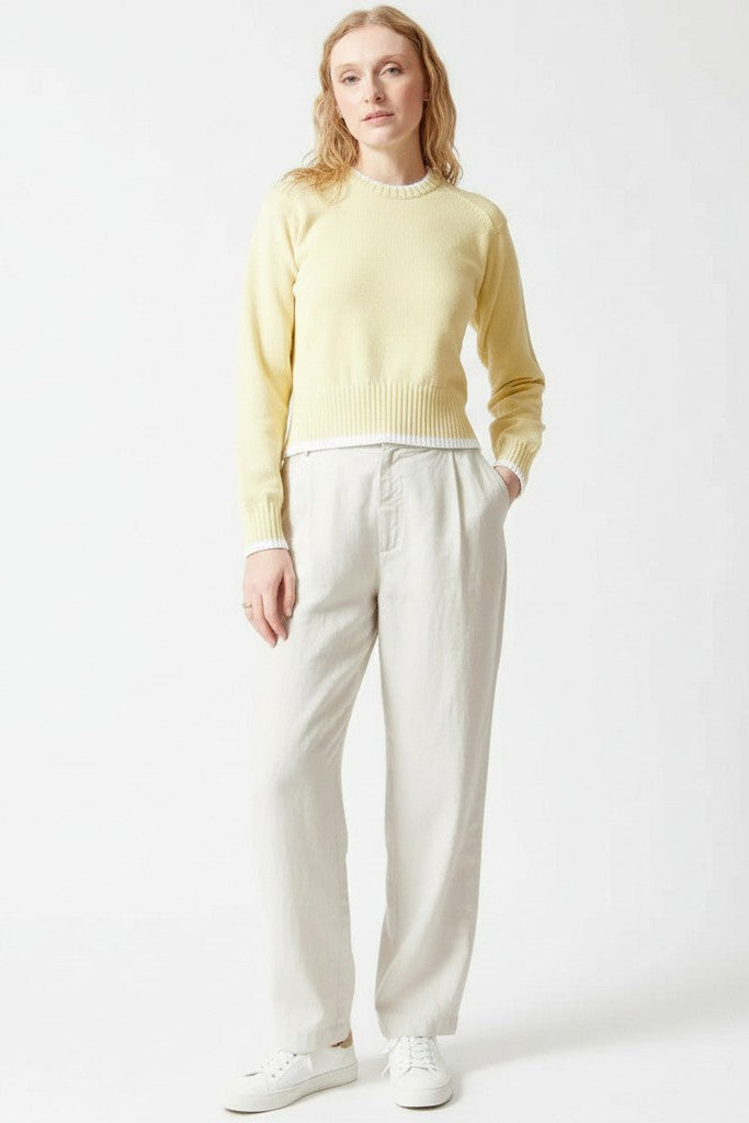 Woman wearing a light yellow sweater and white pants on a white background.