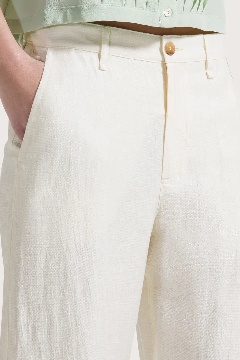 Close-up of a woman wearing light-colored pants with a button detail on a plain background.