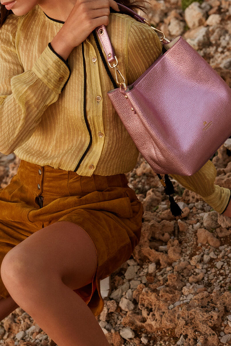 Woman holding a pink handbag on a rocky ground.