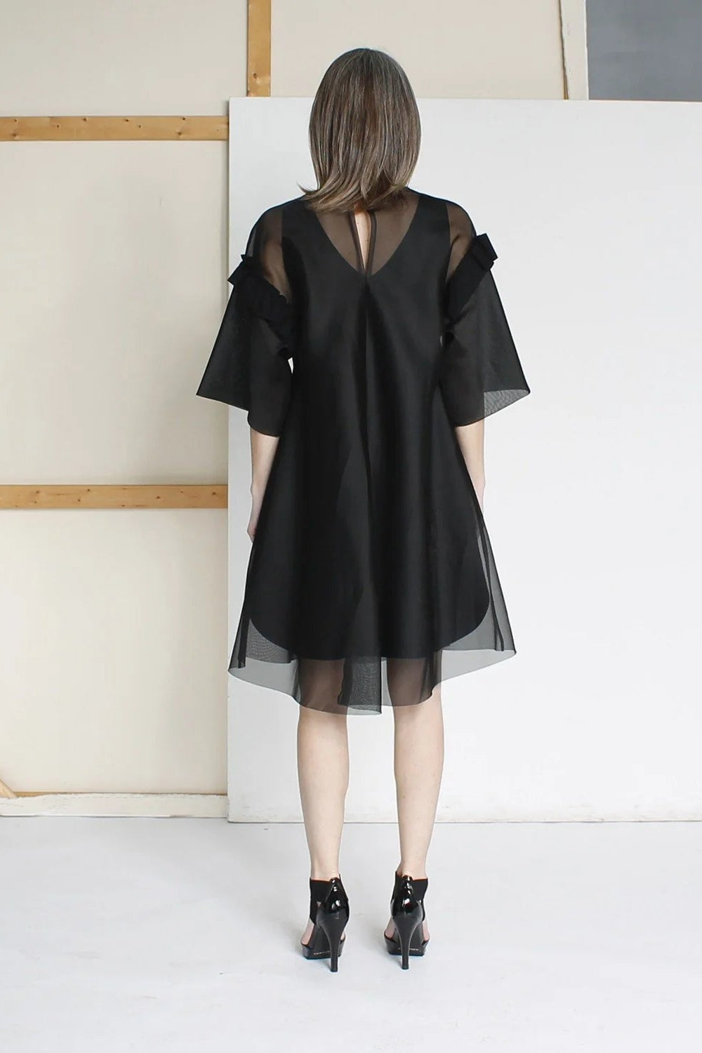The back of a woman wearing a black dress with sheer sleeves.