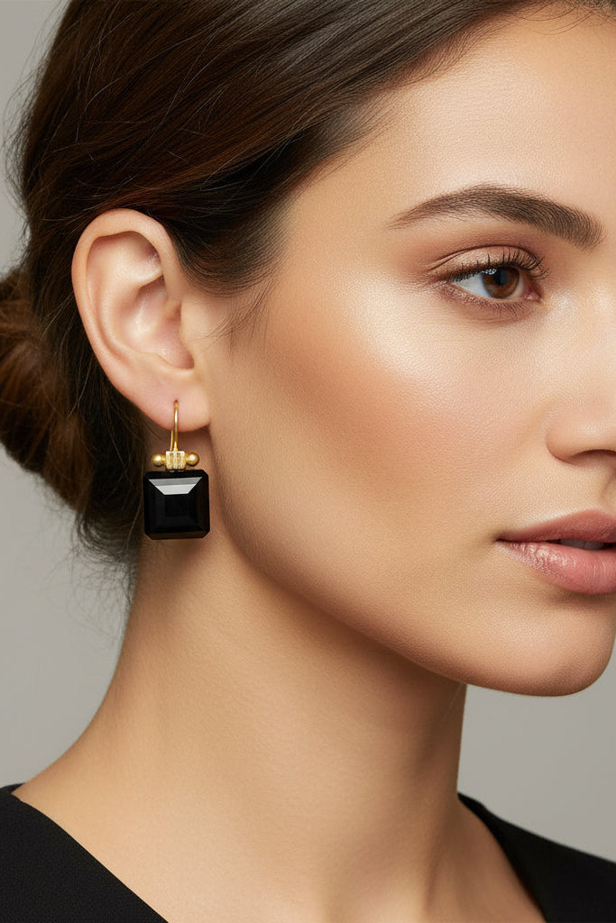 Close-up of a woman wearing black earrings against a neutral background