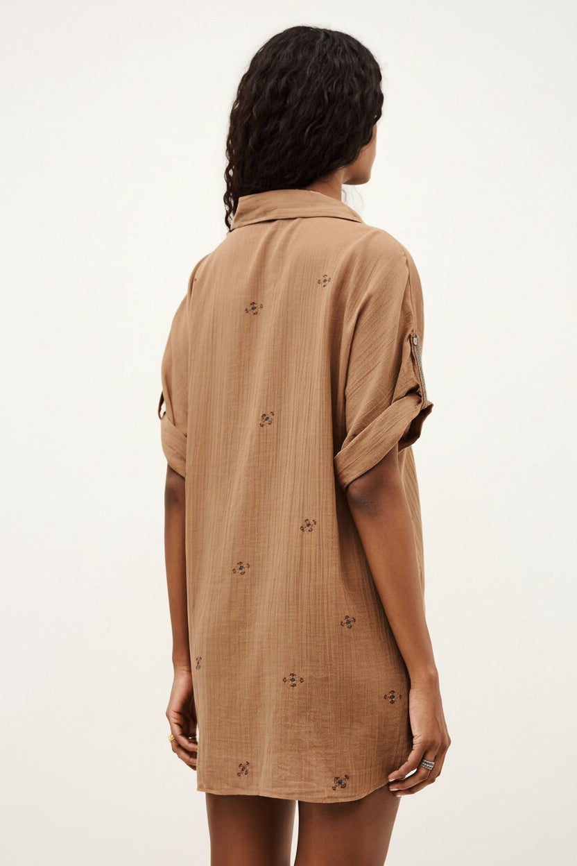 The back of a woman wearing a beige shirt dress with floral patterns on a white background.