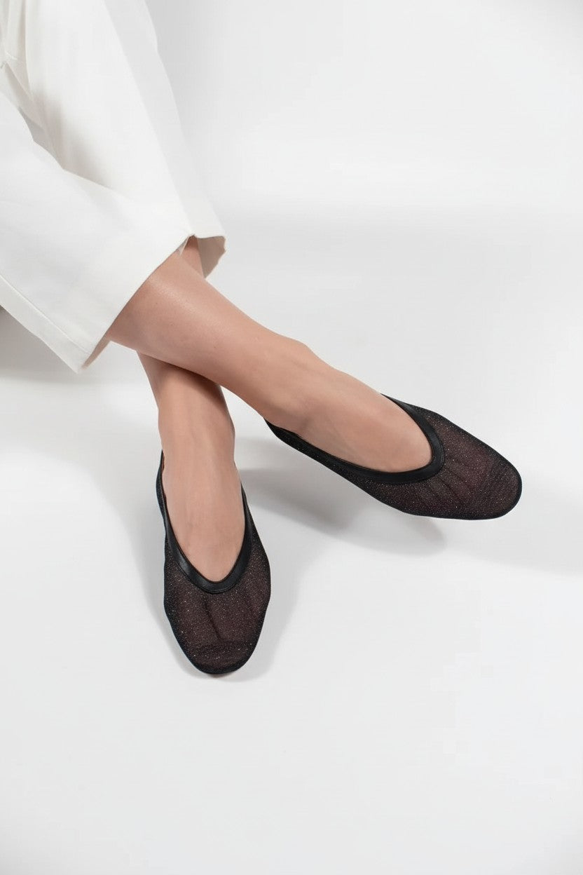 Black flat shoes worn with white pants on a light background.