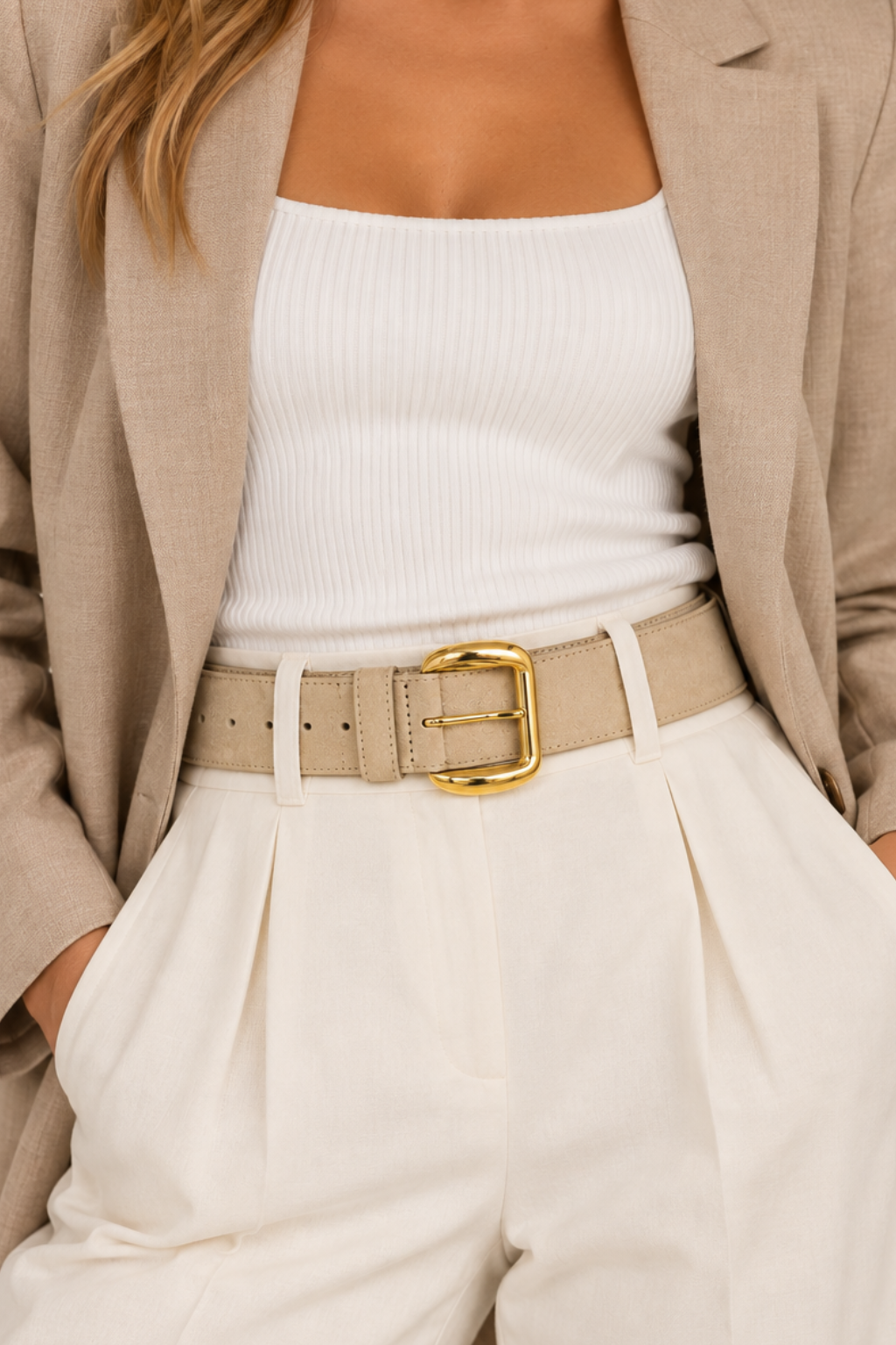 A woman wearing a beige blazer, white ribbed tank top, and white high-waisted trousers with a beige belt featuring a gold buckle.