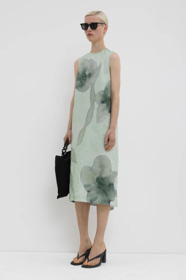 Side view of a woman wearing a green sleeveless dress with floral pattern on a white background.