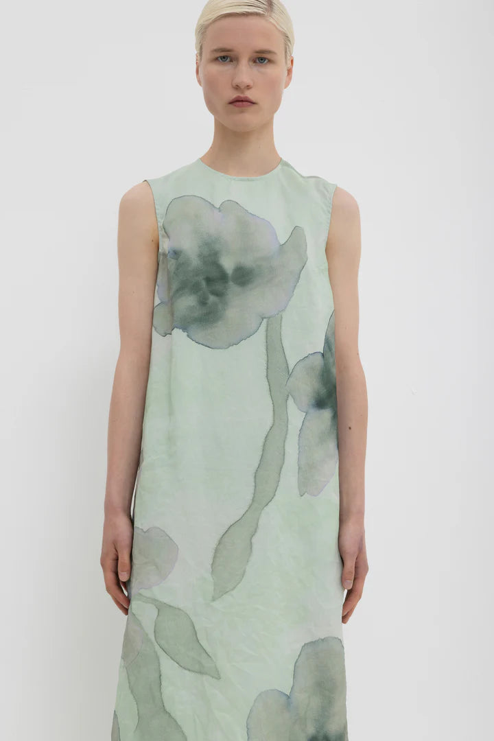Close-up of a woman wearing a green sleeveless dress with floral pattern on a white background.