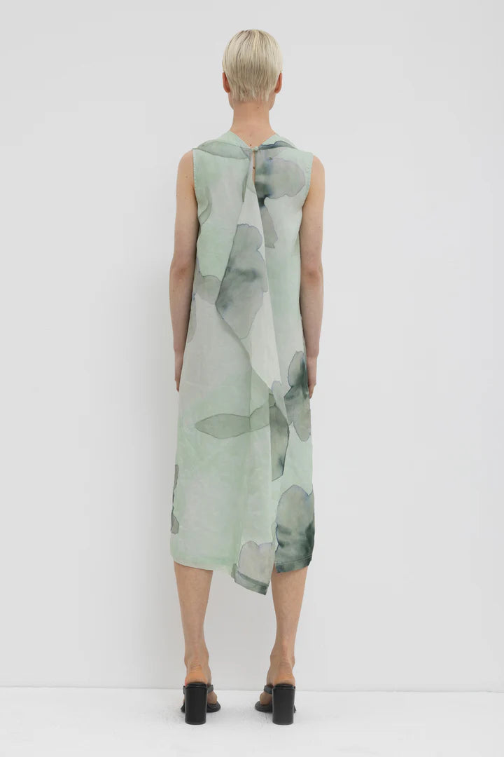 Back of a woman wearing a green floral dress with a plain background.
