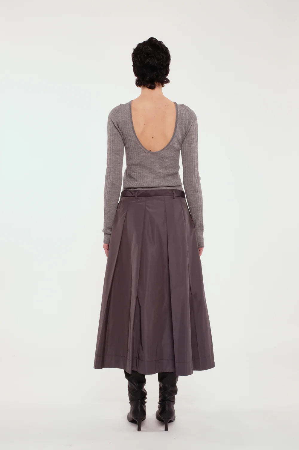 Back of a woman wearing a gray long-sleeve top and brown skirt on a white background.