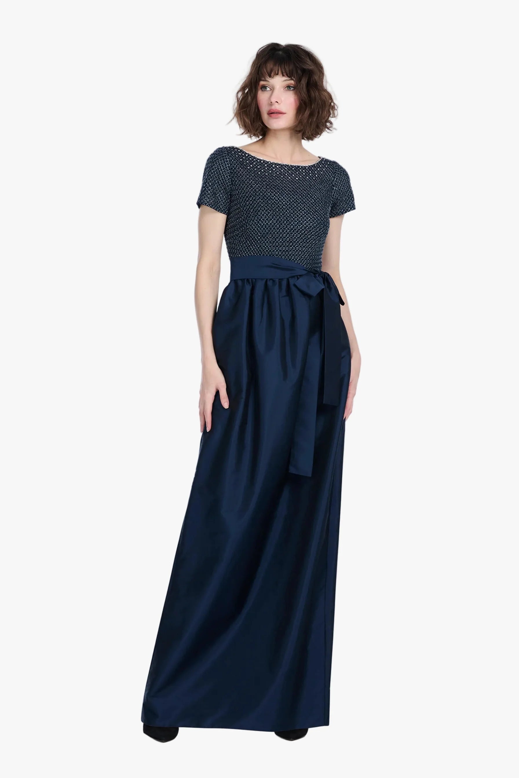 Woman wearing a navy dress with a beaded top on a white background.