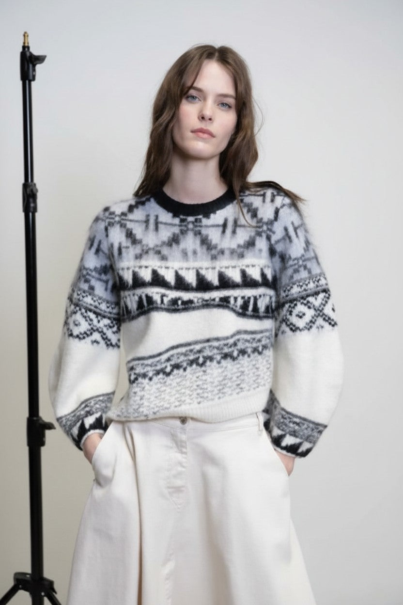 Model wearing a patterned sweater and white pants against a plain background