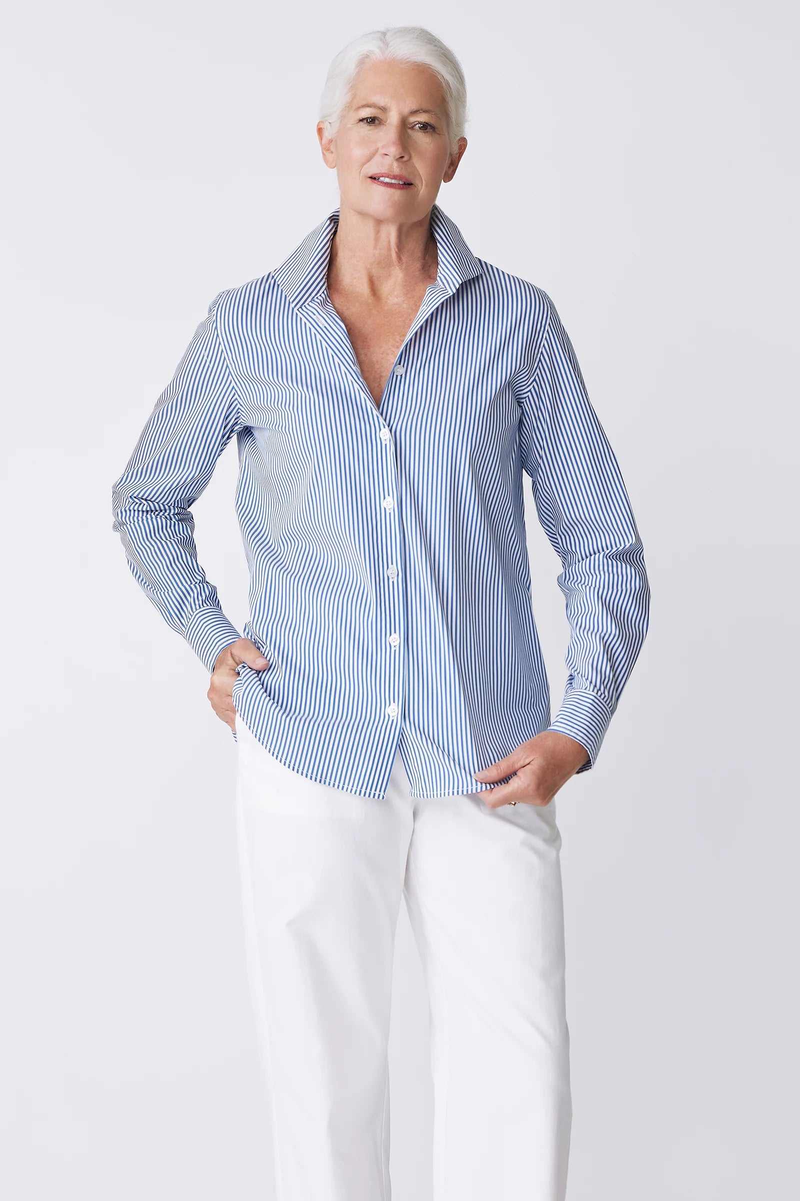 Woman wearing a blue and white striped shirt and white pants on a light gray background.