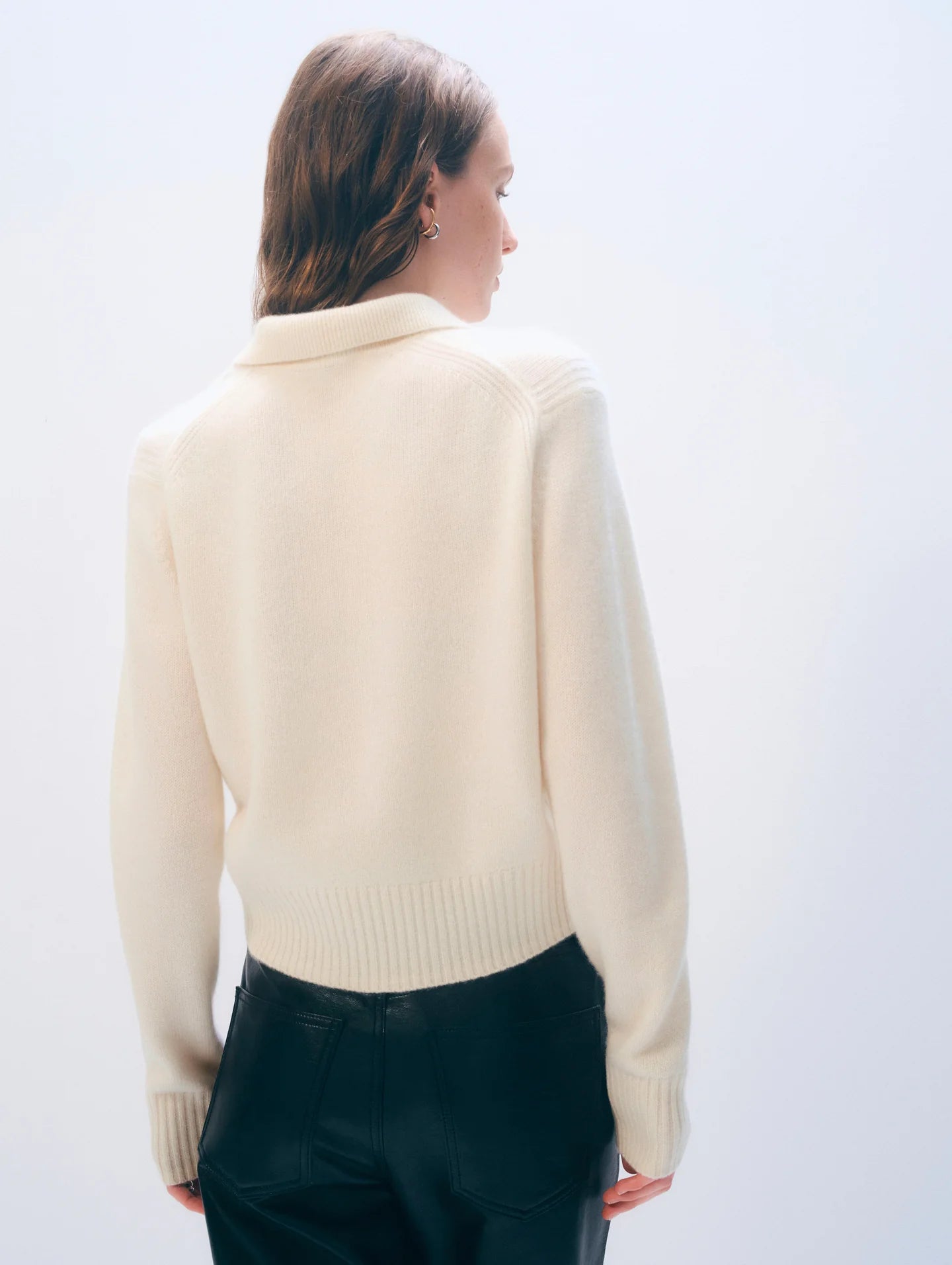 Woman wearing a cream sweater and dark pants against a white background.