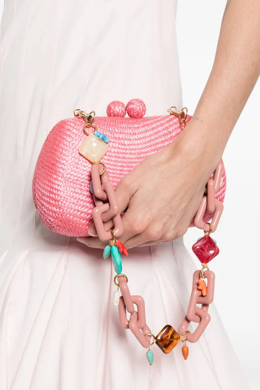 Pink straw handbag with colorful bead embellishments held by a hand against a white background.