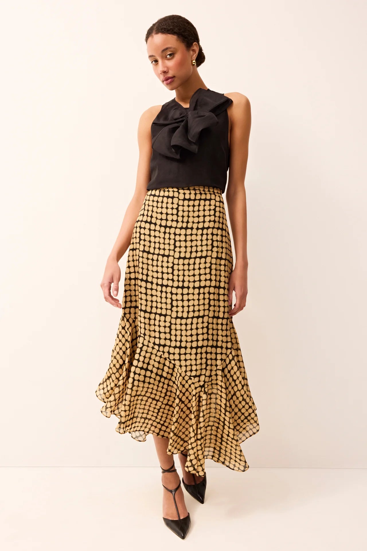 Woman wearing a black top with a bow and a yellow checkered skirt on a white background.