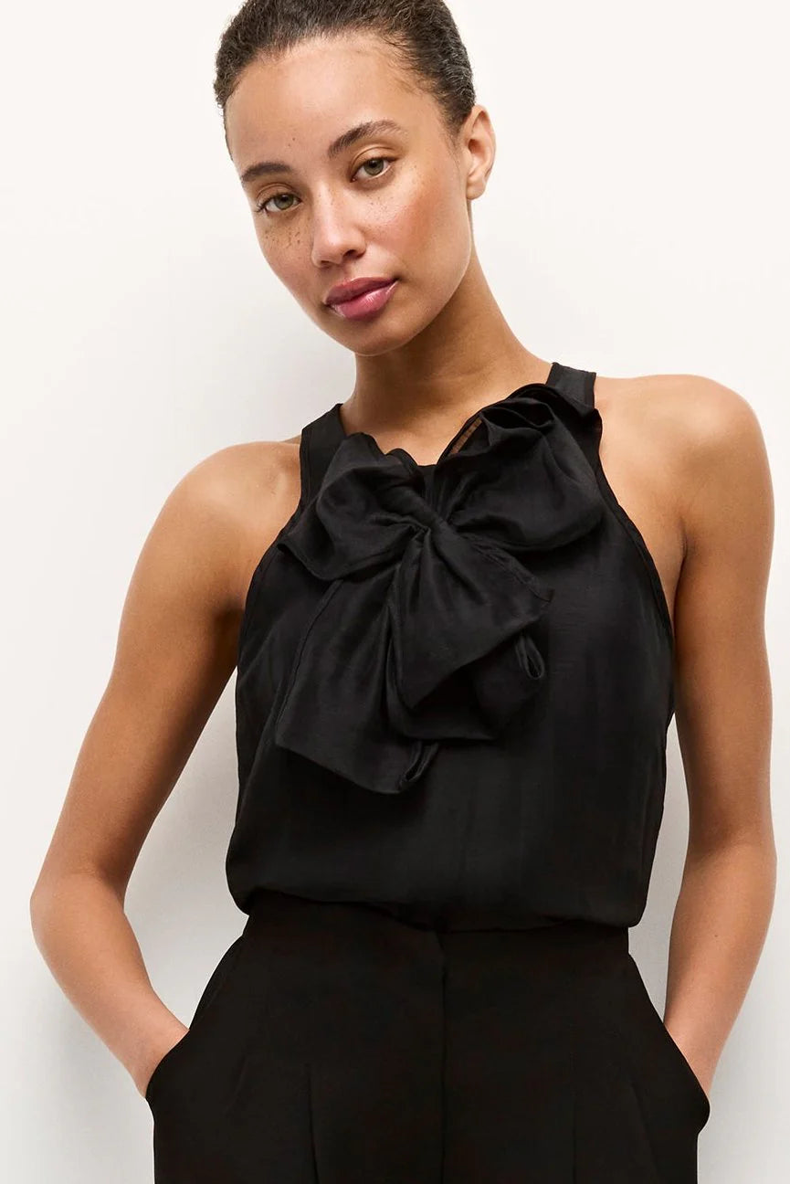 Woman wearing a black sleeveless top with a large bow detail on a white background.
