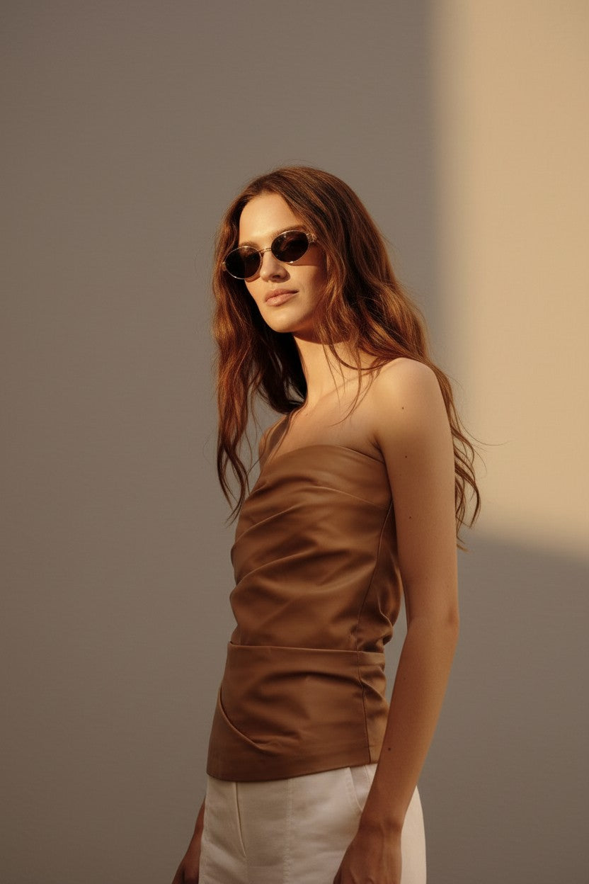 Woman wearing a brown bustier top and sunglasses against a neutral background.