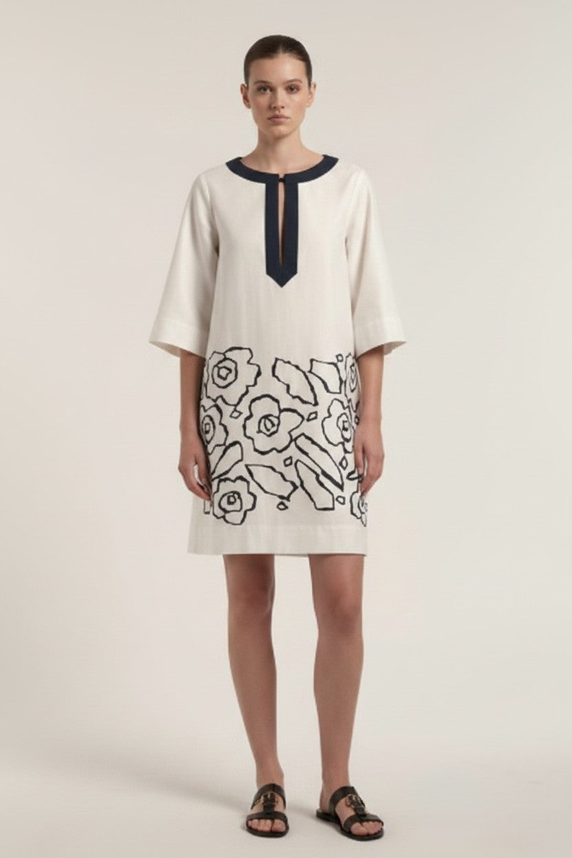 Woman wearing an off-white dress with navy floral patterns on a plain background.