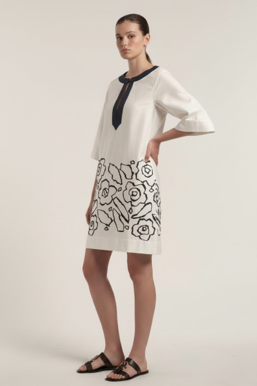 Woman wearing an off-white dress with navy floral patterns on a plain background.