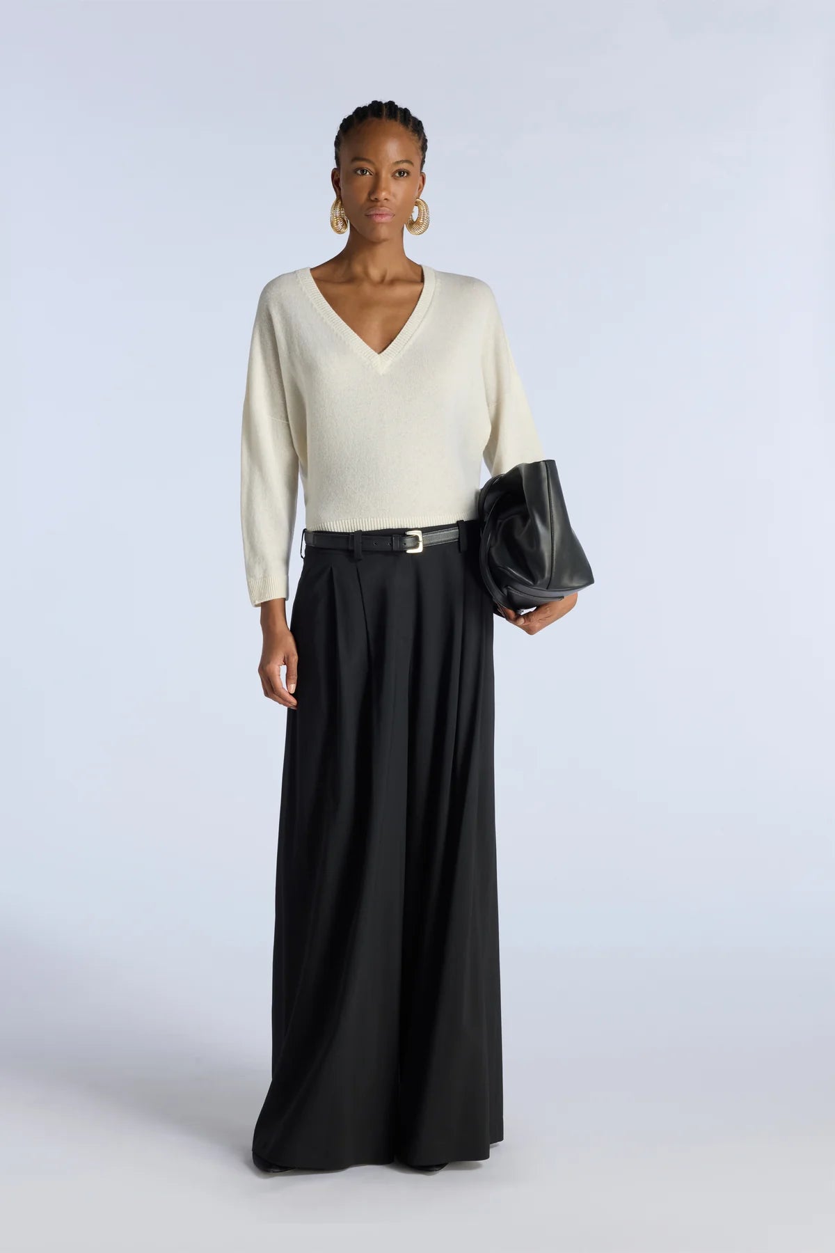 Woman wearing an off white top and black skirt holding a clutch against a white background.