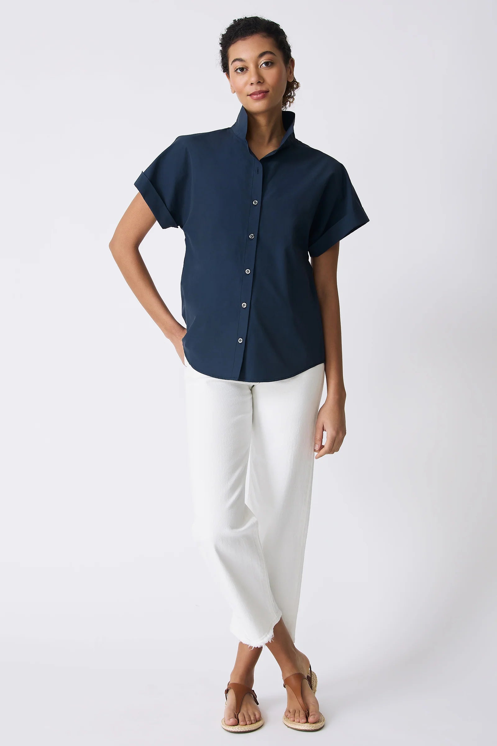 Woman wearing a navy blue short-sleeve shirt and white pants on a white background.