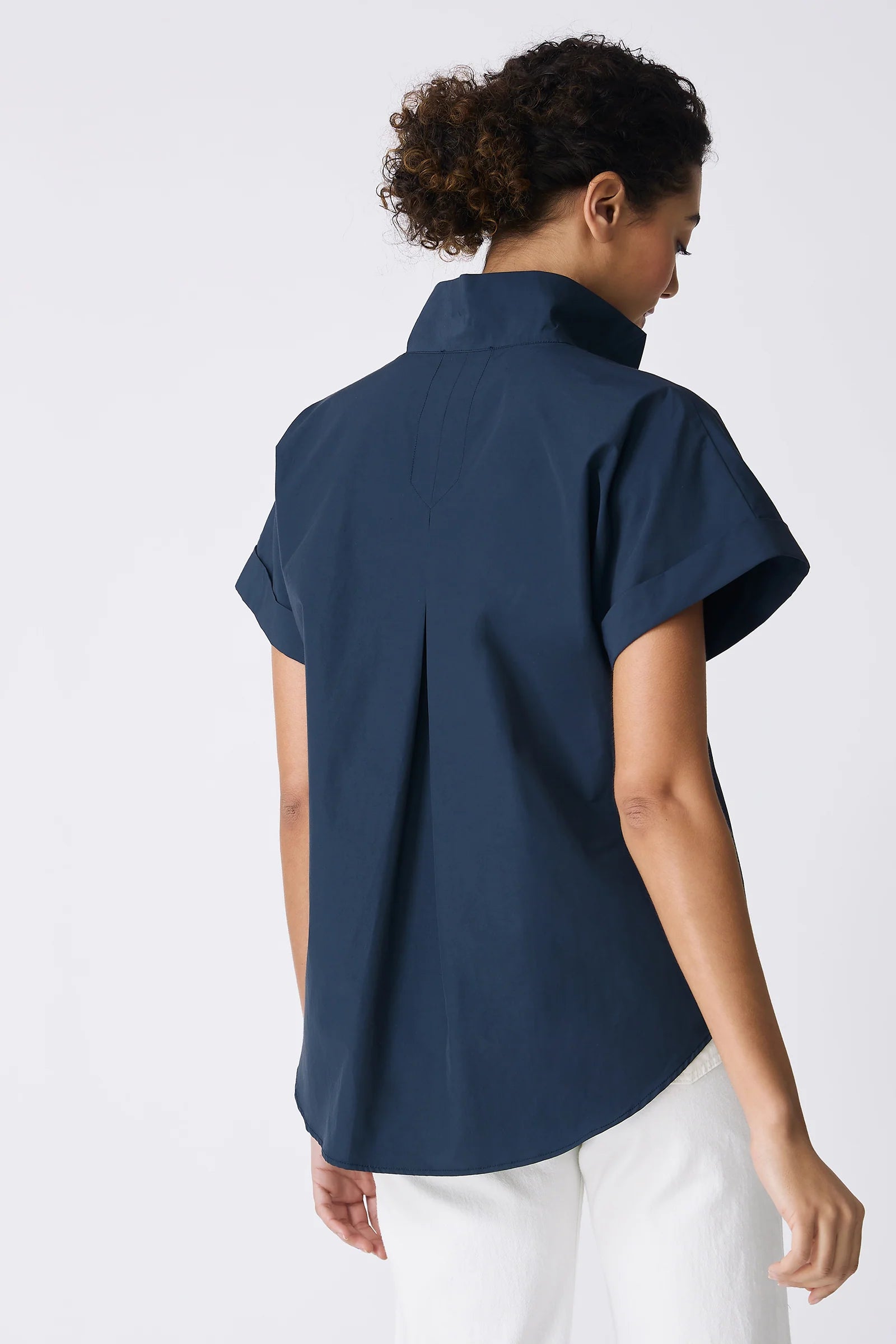 Woman wearing a navy blue shirt and white pants on a light gray background.