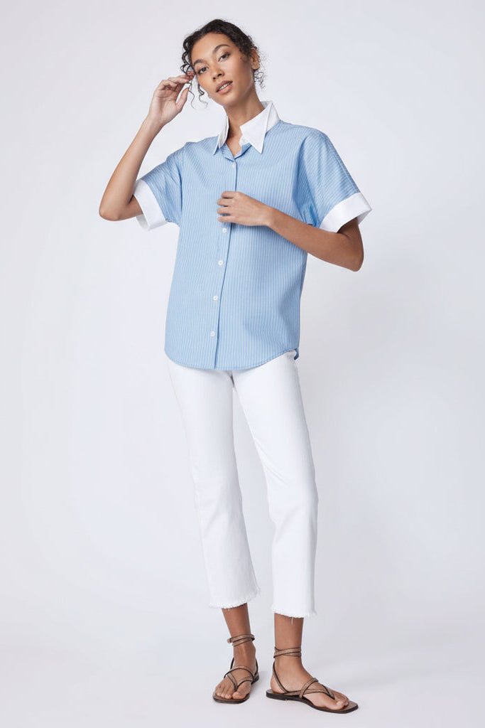 Woman wearing a light blue shirt and white pants on a plain background