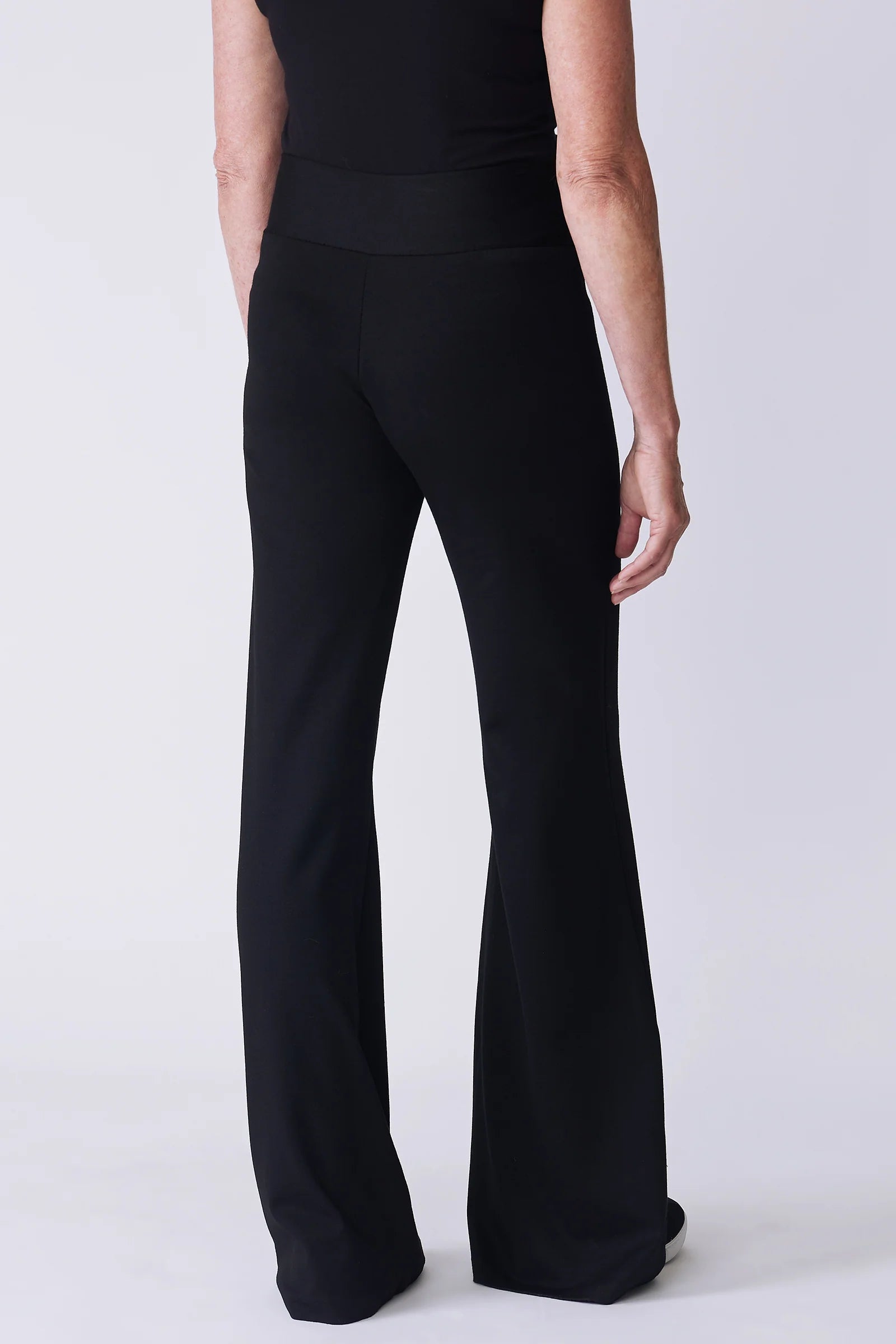 Black wide-leg pants shown from the back on a model, featuring a high-waisted design and a slight flare at the hem, against a light gray studio background.