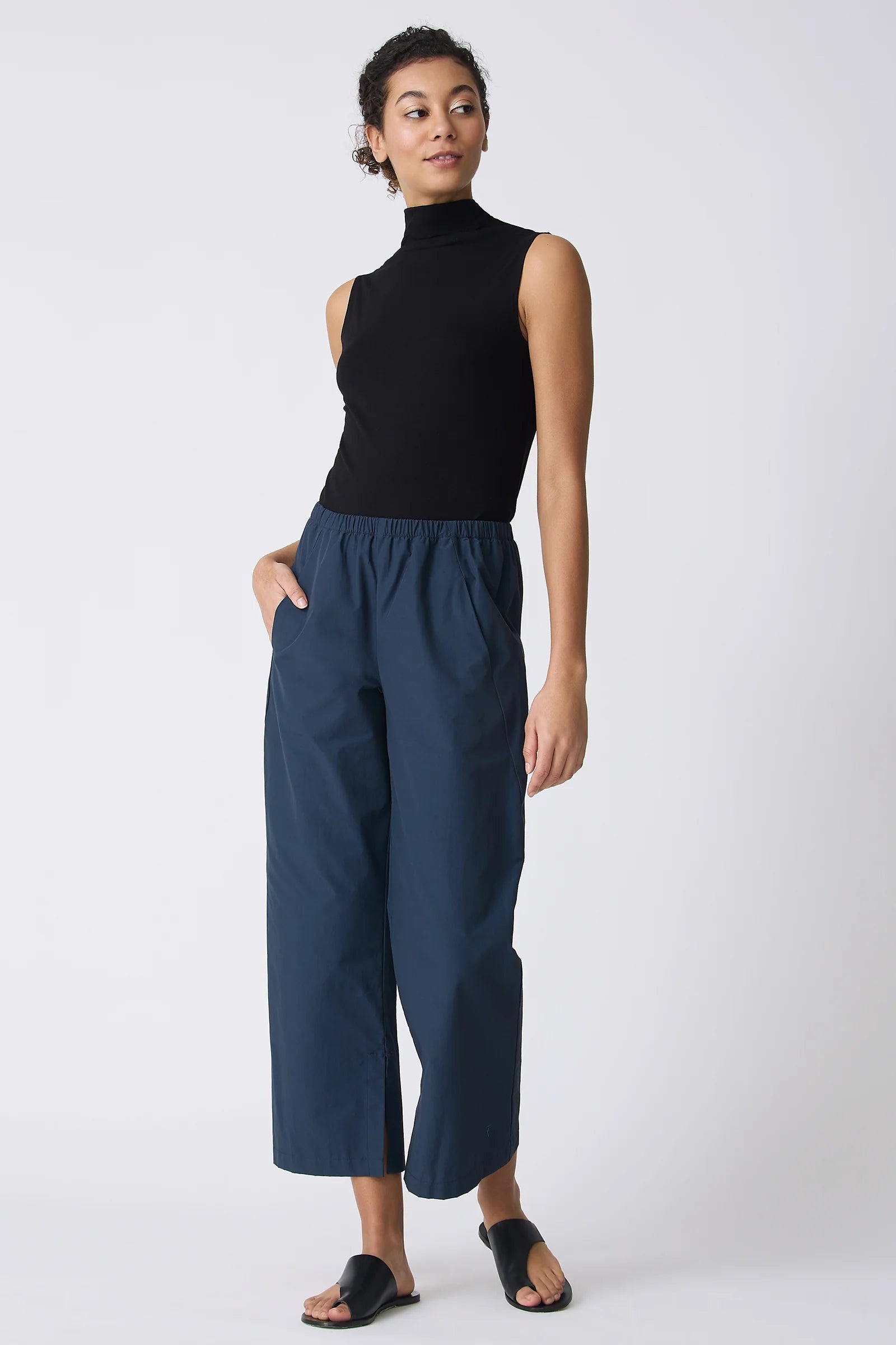 Woman wearing a black sleeveless top and blue pants on a white background.