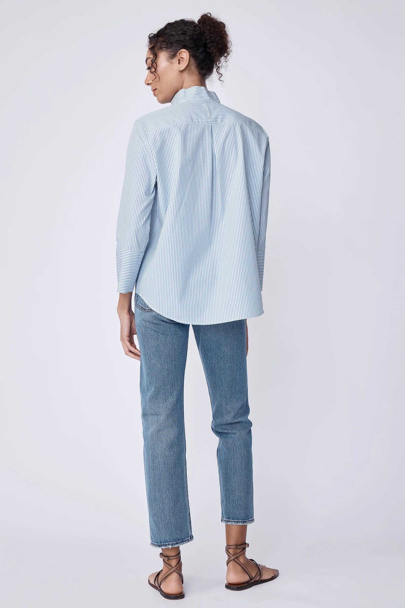 Woman wearing a light blue stripe shirt and jeans on a white background.