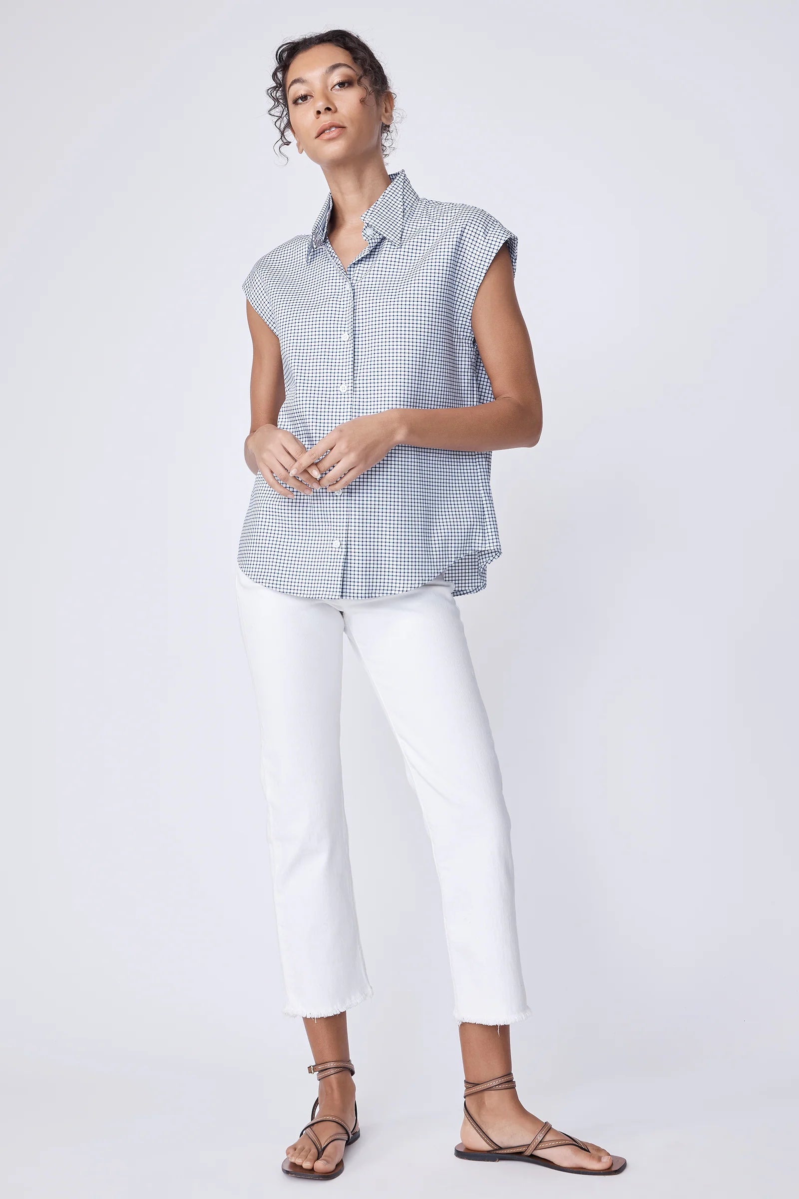 Woman wearing a sleeveless checkered shirt and white pants on a white background.
