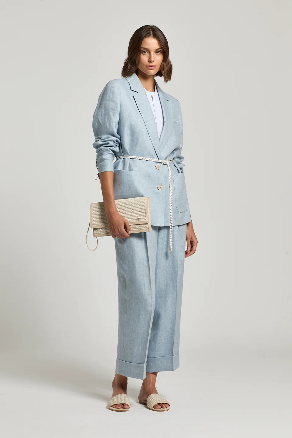 Woman wearing a light blue linen suit holding a clutch against a plain background.